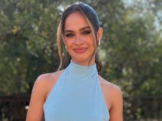 a woman in a light blue dress posing for a photo with trees in the background