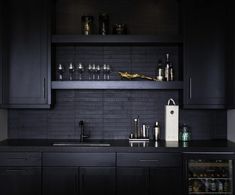 a kitchen with dark cabinets and black counter tops, including a wine cooler in the corner