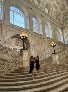 two women are walking down the stairs in an ornate building