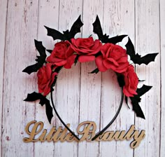 a wreath with red roses and black bats on it that says little beauty in gold lettering