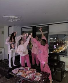 three girls in pink pajamas standing on top of a coffee table with their hands up