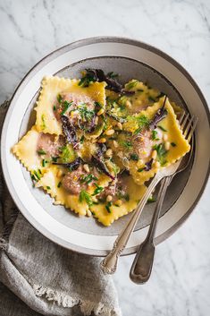 a white bowl filled with pasta and meat on top of a marble table next to a fork