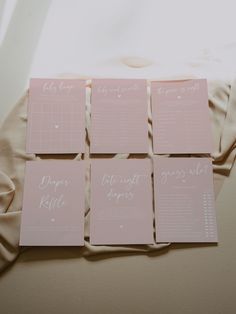 four pink cards with white writing on them sitting on top of a sheet of paper