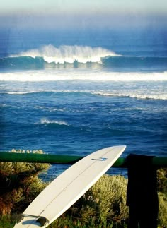 a white surfboard leaning against a fence near the ocean with waves in the background