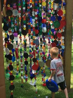 a young boy holding a frisbee in front of a colorful art piece hanging from a wooden structure