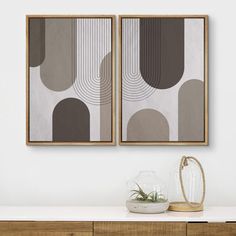 two framed art prints hanging on the wall above a dresser with vases and plants