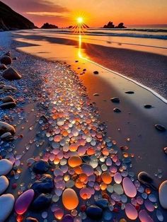 the sun is setting over an ocean with rocks and water on it's shore