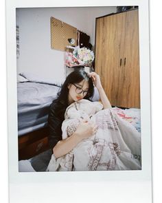 a woman holding a baby in her arms while laying on a bed next to a dresser