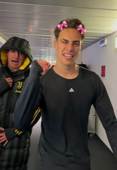 two young men are standing in an office hallway and one is wearing a black jacket