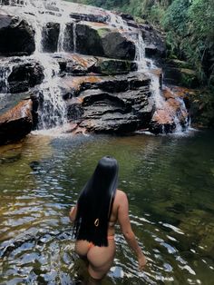 a woman standing in the water next to a waterfall