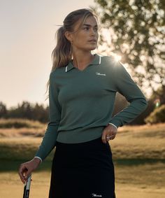 a woman holding a tennis racquet on top of a grass covered golf course