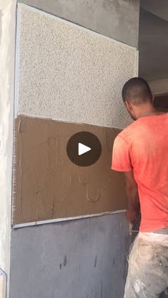 a man in an orange shirt is painting the side of a building with brown paint