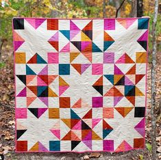 a colorful quilt hanging from a tree in the woods