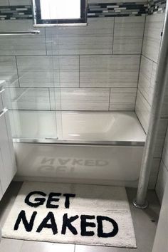 a bathroom with a rug that says get naked on the floor next to a bathtub