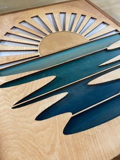 the sun is setting on top of a wooden plaque that has blue and green designs