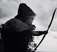 an old man holding a bow and arrow in his hand while standing on the beach