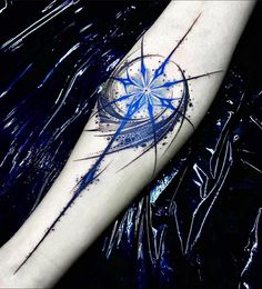 a blue ink splattered arm with a compass tattoo on it's forearm