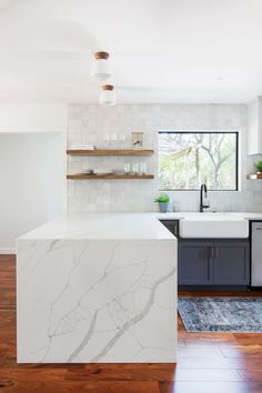 a kitchen with white marble counter tops and wooden floors, along with open shelving above the sink