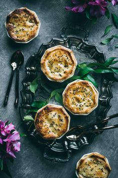 three small pies sitting on top of a metal plate next to purple flowers and silverware