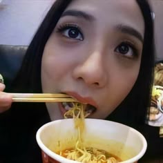 a woman eating noodles with chopsticks in her mouth