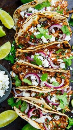 several tacos with meat, onions and cilantro on a black surface next to limes