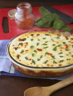 a casserole dish with cheese and herbs in it on a table next to a spoon