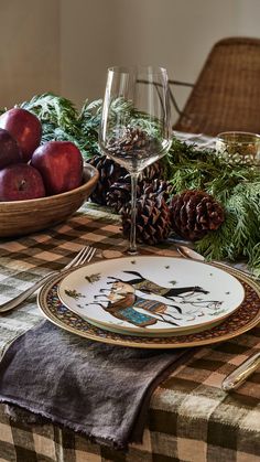 a table topped with plates and glasses filled with fruit next to pine cones, evergreen branches