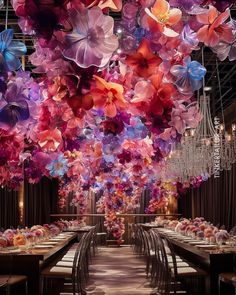 a room filled with lots of tables covered in purple and pink paper flowers hanging from the ceiling