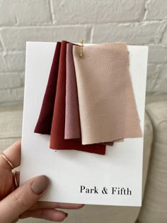 a person holding up some fabric samples in front of a white brick wall with the words park and fifth written on it