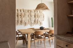 a dining room table and chairs in front of a wall hanging with tassels