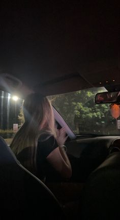 a woman sitting in the passenger seat of a car at night talking on her cell phone