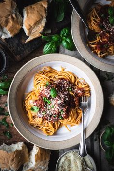 two plates of spaghetti with meat sauce and parmesan bread on the side next to them