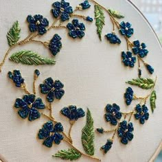 blue flowers and green leaves are embroidered onto a white cloth with gold trimmings