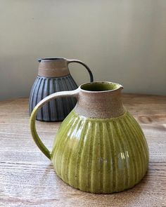 two green and black vases sitting on top of a wooden table next to each other