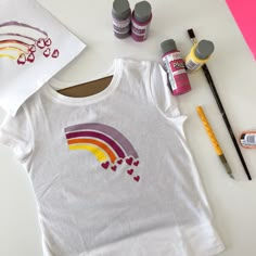 a t - shirt with hearts and rainbows painted on it next to markers, paintbrushes