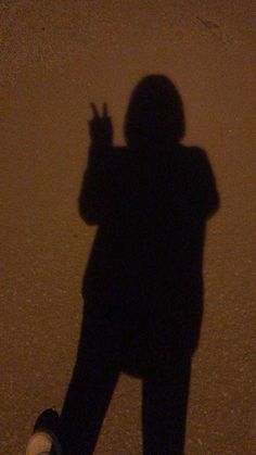 the shadow of a person standing in front of a wall holding a cell phone up to their ear