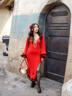 a woman in a red dress standing next to a door and holding a handbag