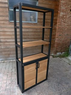 a wooden and metal shelving unit sitting on the side of a brick road next to a building