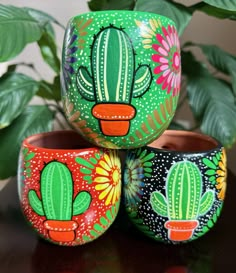 three hand painted cactus pots sitting on top of a wooden table next to a potted plant