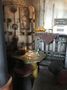 a table and stools in a room with pipes on the wall, and an oven behind it