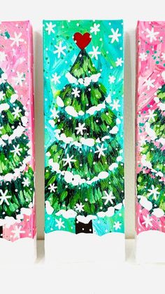 three christmas trees painted with acrylic paint on canvases in pink, green and blue