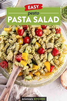 pasta salad with pesto and tomatoes in a glass bowl on top of a white table