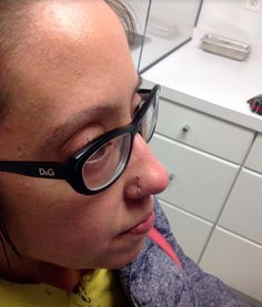 a woman with glasses on her face and tongue sticking out from under the nose, in front of a white cabinet