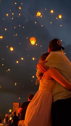 two people embracing each other in front of many lit lanterns flying above them at night