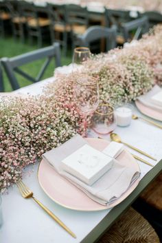 the table is set with pink and white plates, silverware, and baby's breath flowers