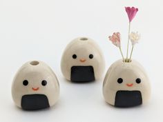 three small ceramic vases with flowers in them on a white table top, one has a flower sticking out of it's mouth