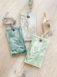 three ceramic tags on a wooden table with ribbons hanging from the top and two are decorated with leaves