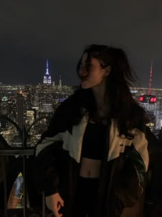 a woman standing on top of a building at night with the city lights in the background