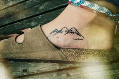 a woman's foot with a mountain tattoo on her left ankle and the mountains behind her