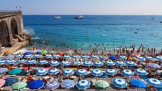 many people are on the beach with umbrellas and boats in the water behind them